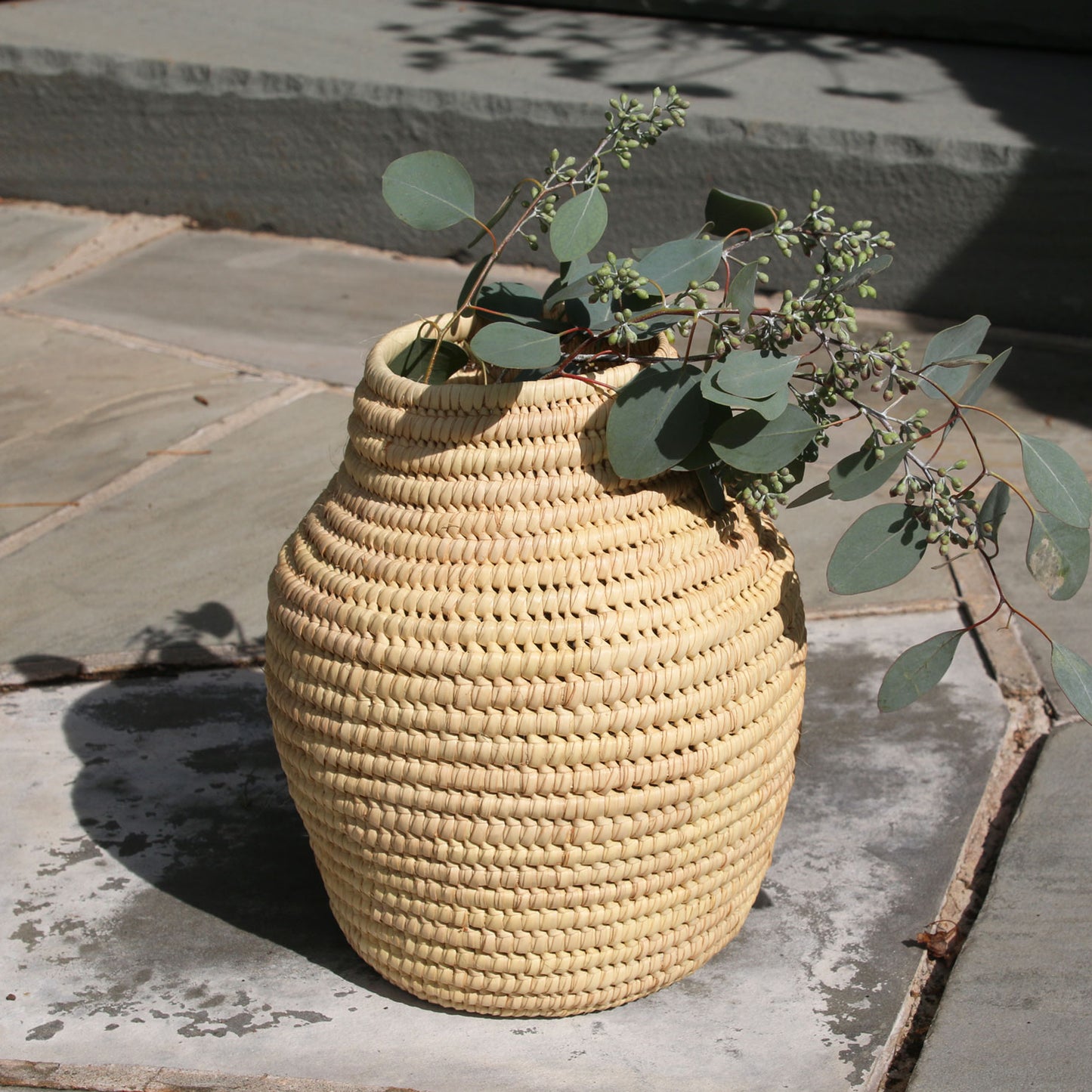 Woven beige vase with greenery on a stone surface