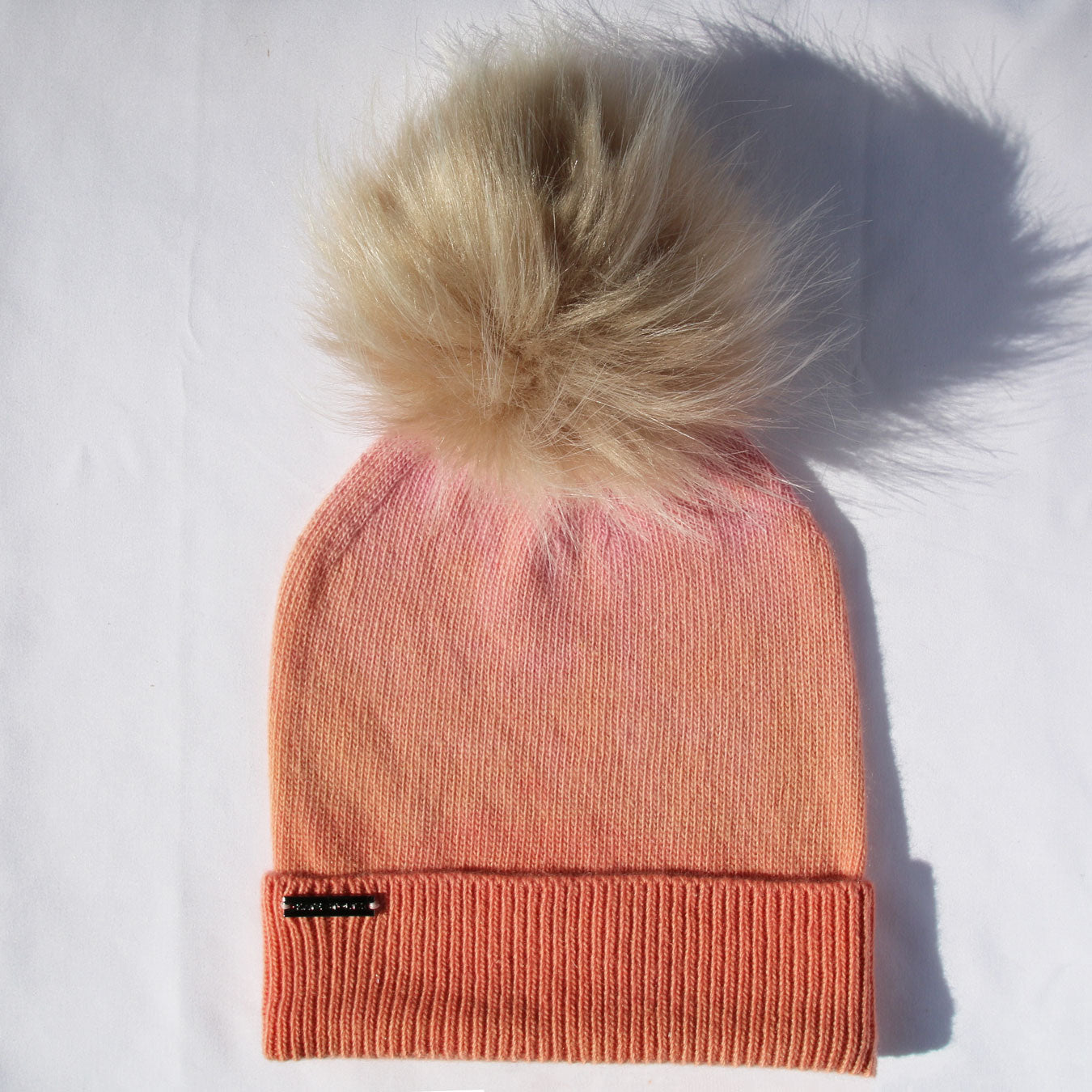 Pink knit beanie with a large fur pom-pom on a white background